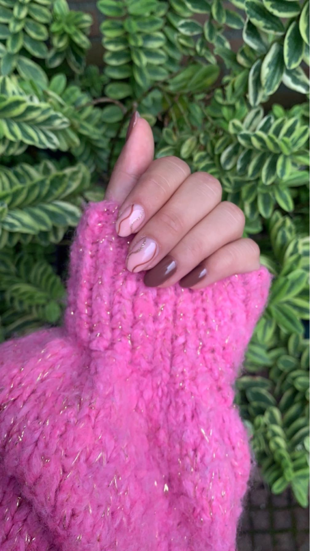 Mauve en bruine nagels boven een roze gebreide trui